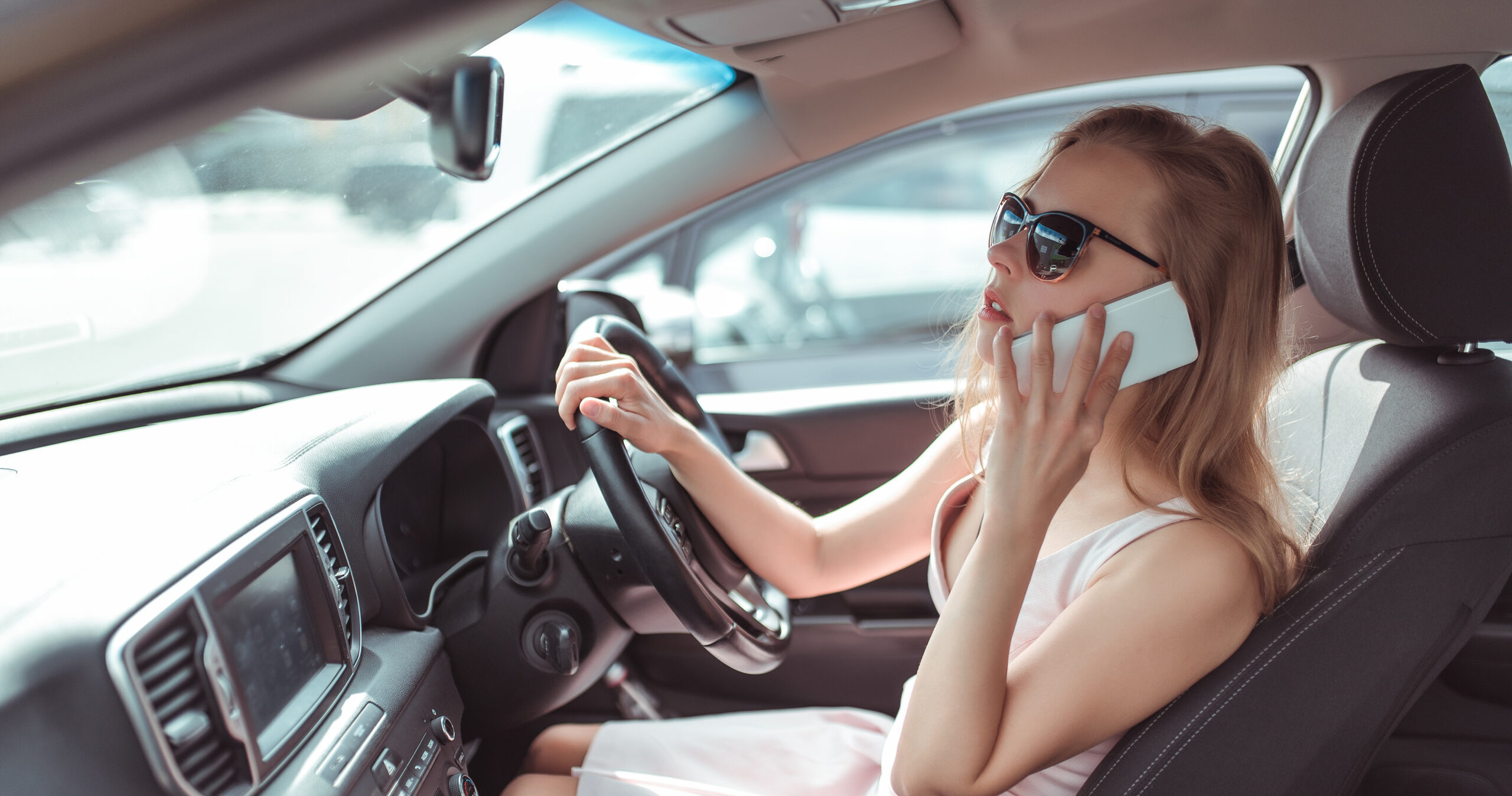 woman makes phone call, in summer city parking lot near shopping center, reversing in parking lot. Pink dress sunglasses listening to message on cell phone.